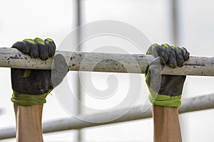 Close-up of muscular worker hands hanging on scaffold metal pipe on white house wall with polyurethane foam sheet background. Mode