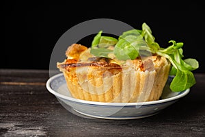 Close-up of mushroom quiche with lamb`s lettuce, selective focus, on dark wooden table, black background, horizontal