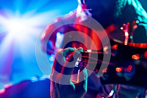 Close-up of musician& x27;s fingers on bass guitar fretboard playing melodic chords against vibrant light show. Music