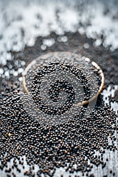 Close up of mustard seeds/Rai or brown mustard seeds in a small plate on a wooden surface in dark Gothic colors.