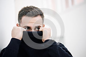 Close-up of a mysterious man partially hiding his face behind a black turtleneck