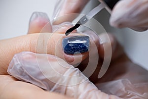 Close-up of a nail on which a blue gel polish is applied distributing it with a manicure brush over the surface