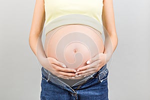 Close up of naked pregnant woman`s belly wearing opened jeans at colorful background with copy space. Pregnancy concept