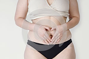 Close-up of a natural woman in underwear creating a heart shape on her hips. A plump girl who promotes a positive