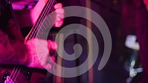 Close-up of the neck of an electric guitar and the hands of the guitarist playing a solo. Purple light from stage