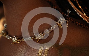 Close up of the neck and shoulder of an African American woman wearing a gold necklace and streaks of liquid gold