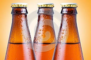 Close-up of the necks of three wet glass brown bottles of dark beer on a yellow background. Alcoholic beverages