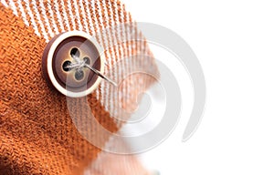 Close up of needle with brown thread and brown sewing button on a shirt.