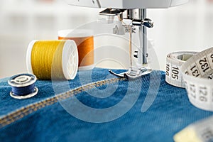 Close up of needle of sewing machine on the denim fabric stitch, threads and measuring tape