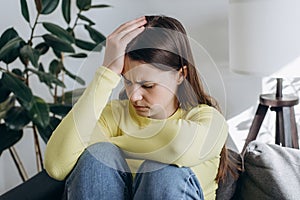 Close up of nervous young caucasian woman sitting alone on couch at home feeling sad tired and worried suffering depression in