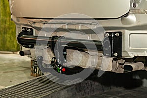 Close-up on a new black tow hitch installed on a modern car with a beige-colored bumper removed in a vehicle repair shop. The