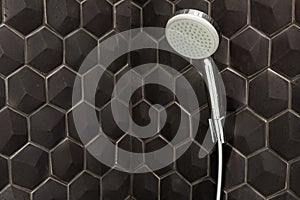 Close up of new rain shower head in the bathroom against a background of black tiles.