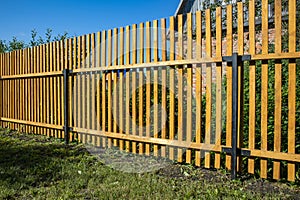 Close-up of a new wooden picket fence in the backyard of a country house, a sunny summer day