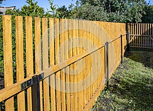 Close-up of a new wooden picket fence in the backyard of a country house, a sunny summer day