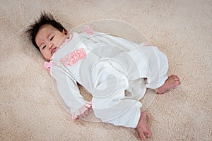 Close up A newborn Asian girl lies in a white dress on the bed waiting for her mother to take care of her. The little boy rolled