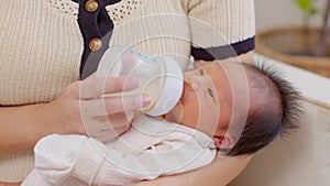 Close up Newborn baby drinking milk from bottle on mom arms.Beautiful Asian mother holding infant baby feeding milk with love at