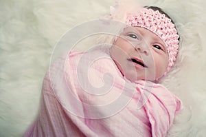 Close up of newborn baby girl in pink with funny expression.