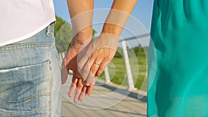 CLOSE UP: Newly engaged couple holds hands while on a romantic stroll in park.