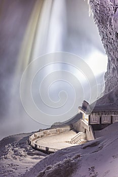Close up of Niagara Falls frozen during a winter storm lit up at night with snow and ice covering a viewing platform