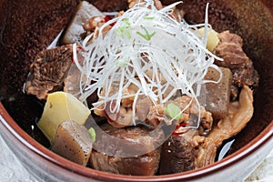 Close-up Nikujaga including beef, potato and radish stew topping with sliced radish and scallion in brown ceramic bowl on makisu.