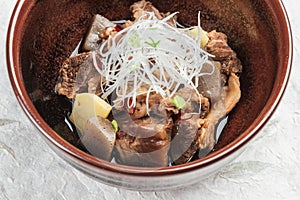 Close-up Nikujaga including beef, potato and radish stew topping with sliced radish and scallion in brown ceramic bowl on washi.