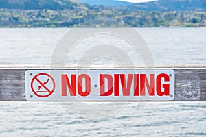 Close-up of No Diving sign on pier with view of Okanagan Lake and mountains in background