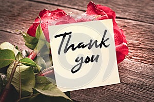 Close-up note with the words Thank you on a bouquet of red roses on a wooden background: the concept of gratitude and appreciation