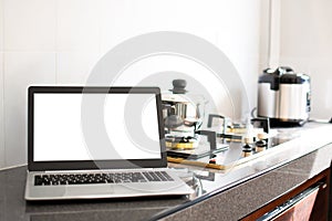 Close up, A notebook computer white screen on the kitchen counter. Has a pot on the gas stove. Blurred background, moke up,