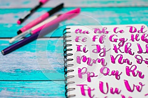 Close up of notebook with hand drawn abc alphabet letters and colorful pens on blue wooden desk background