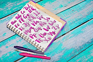 Close up of notebook with hand drawn abc alphabet letters and colorful pens on blue wooden desk background