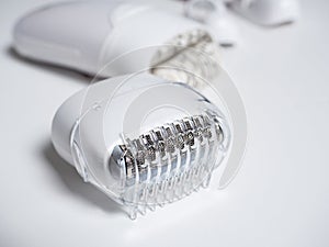 Close-up of the nozzle for a white electric epilator on a white background. In the background, the epilator itself and other