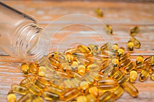 Close up nutritional supplement gold capsules spilled out of clear bottle on wooden table in selective focus