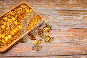 Close up nutritional supplement gold capsules in wooden plate on wooden table in selective focus