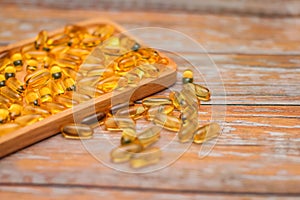 Close up nutritional supplement gold capsules in wooden plate on wooden table in selective focus