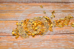 Close up nutritional supplement gold capsules on wooden table in selective focus