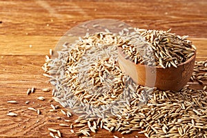 Close-up oat groats heaped in a wooden bowl on rustic wooden background, selective focus.