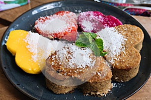 Close up Oatmeal Pancakes and tropical fruits in the form of a heart with mint and honey on wooden table. Valentine