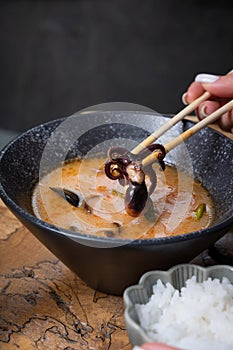 Close up octopus in chopsticks on the background of tom yum soup