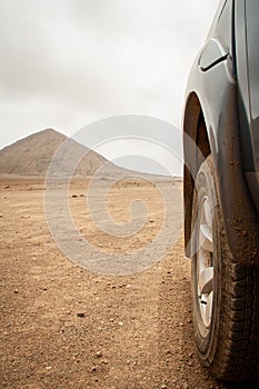 Close Up of the off-road tires dirty with sand, desert of Sal Island, Cape Verde. On background Pico do Fogo, Volcano