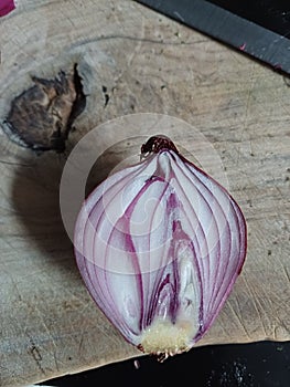 Close up off a splitted purple onion on an olive wood chopping board featuring a sharp Japanese blade in the background