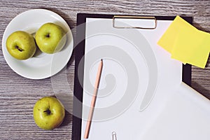 Close up of office accessorise: clipboard, a plate of apples, blank notepad on a wooden background. Weight loss starving dieting s