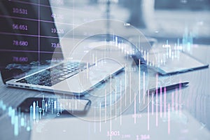 Close up of office desktop with devices, supplies and glowing candlestick forex chart on blurry background. Investment, profit and