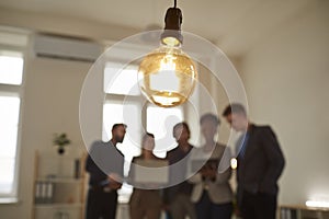 Close up of office light bulb, with team of business people discussing ideas in background