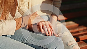 Close up oh female hands of two lesbian girls sitting outdoors. Caring young woman holding hand supporting her