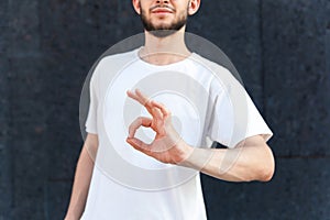 Close-up of the okie sign by the hands of a European bearded man in a white T-shirt outdoors