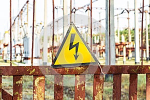 Close-up old aged rusty triangle metal plate with High voltage warning sign. Power station with transformers and