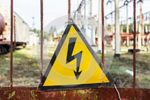 Close-up old aged rusty triangle metal plate with High voltage warning sign. Power station with transformers and