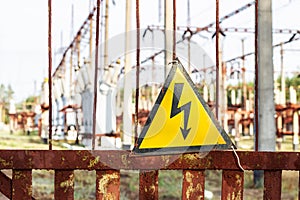 Close-up old aged rusty triangle metal plate with High voltage warning sign. Power station with transformers and electricity