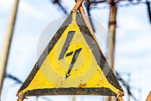 Close-up old aged rusty triangle metal plate with High voltage warning sign. Power station with transformers and electricity distr