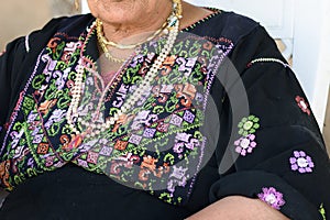 Close up of old Arab woman with traditional arabian dress sitting on chair.